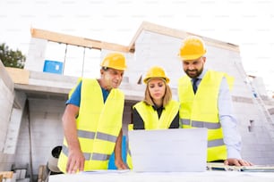 Architect, civil engineer and worker with a laptop, discussing issues at the construction site.