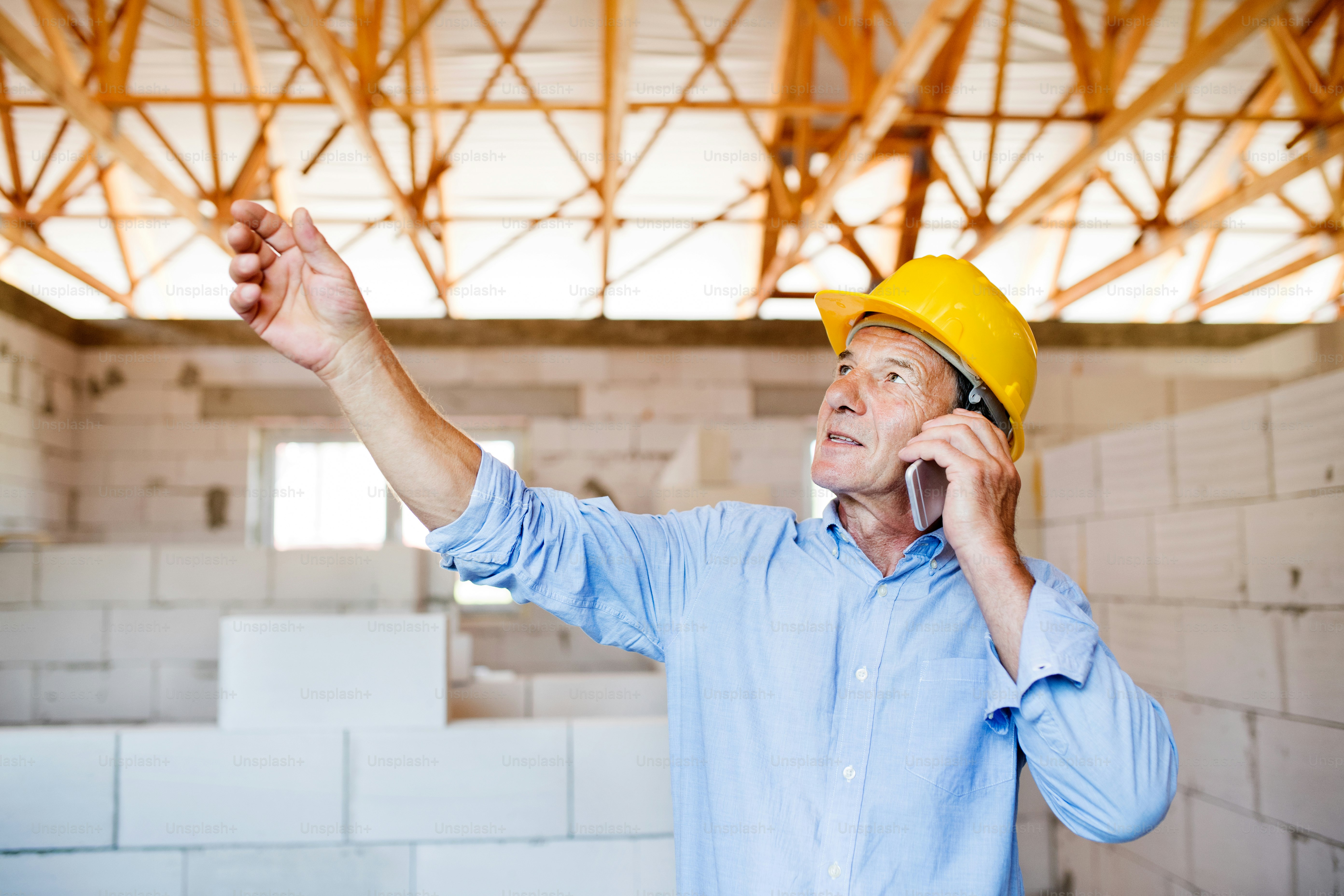Leitender Architekt mit Smartphone auf der Baustelle telefoniert.