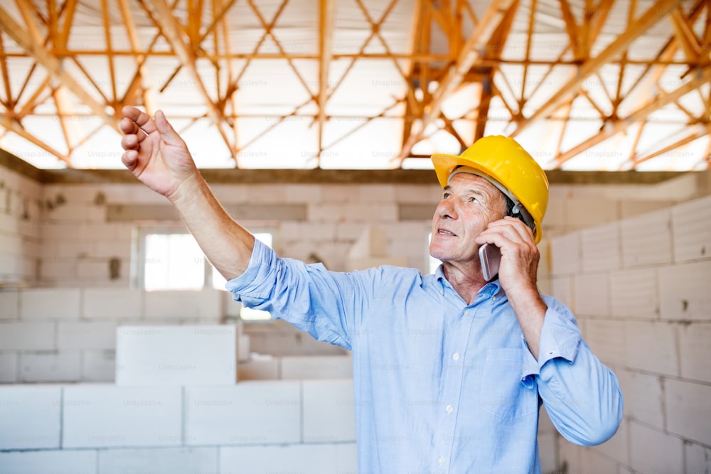 Architecte senior avec smartphone sur le chantier de construction en train de passer un appel téléphonique.