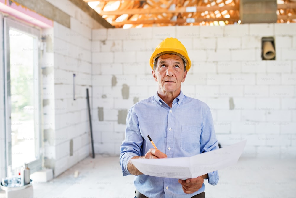 Senior architect or civil engineer at the construction site looking at blueprints, controlling issues at the construction site.