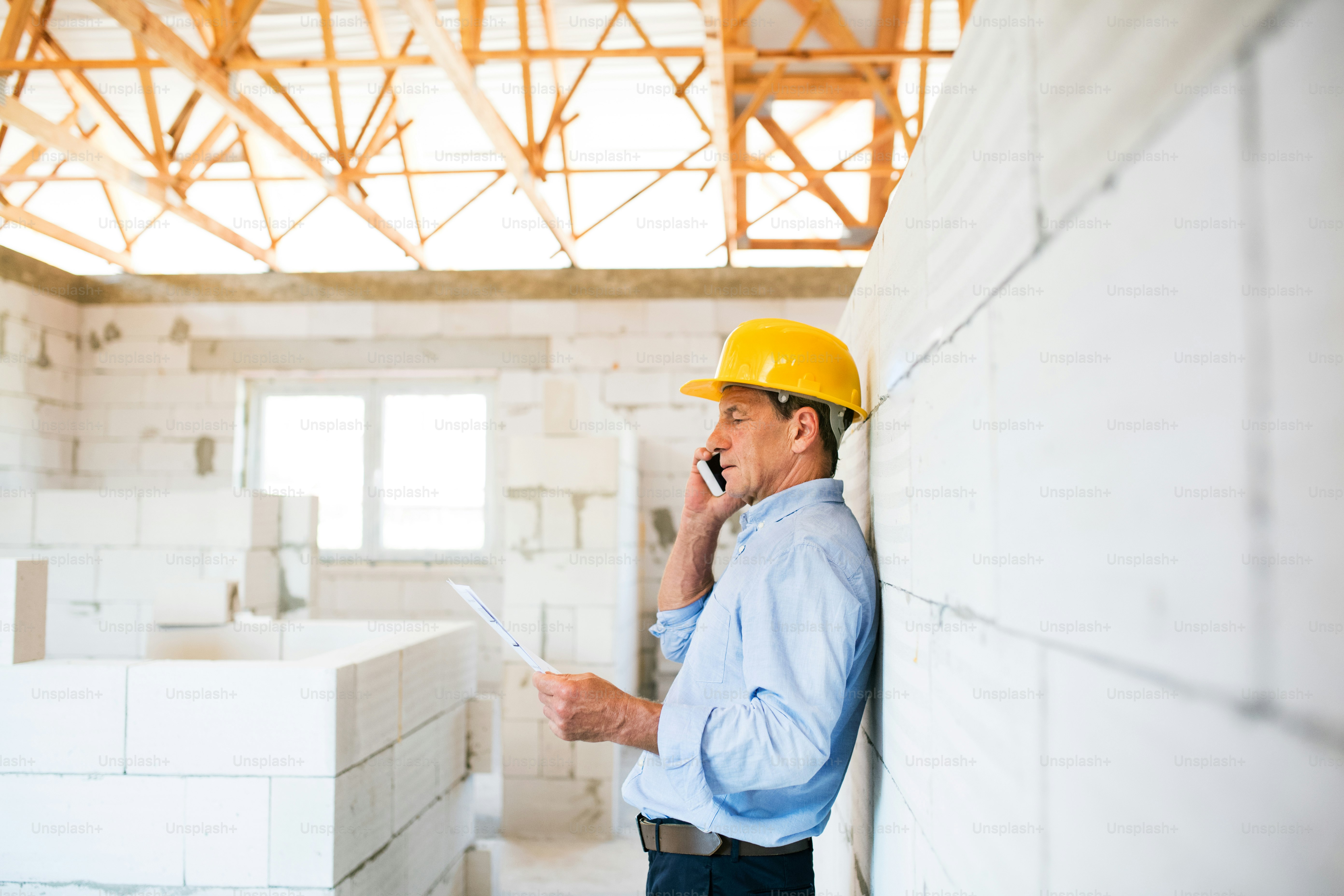 Leitender Architekt mit Smartphone auf der Baustelle telefoniert.