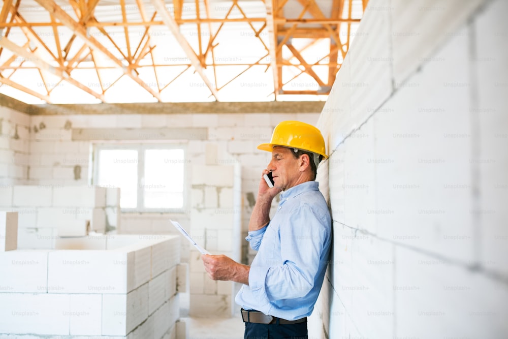 Architecte senior avec smartphone sur le chantier de construction en train de passer un appel téléphonique.