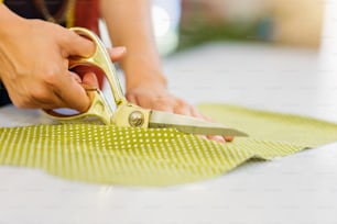 Close up of hands of unrecognizable tailor woman cutting green dotted fabric with scissors