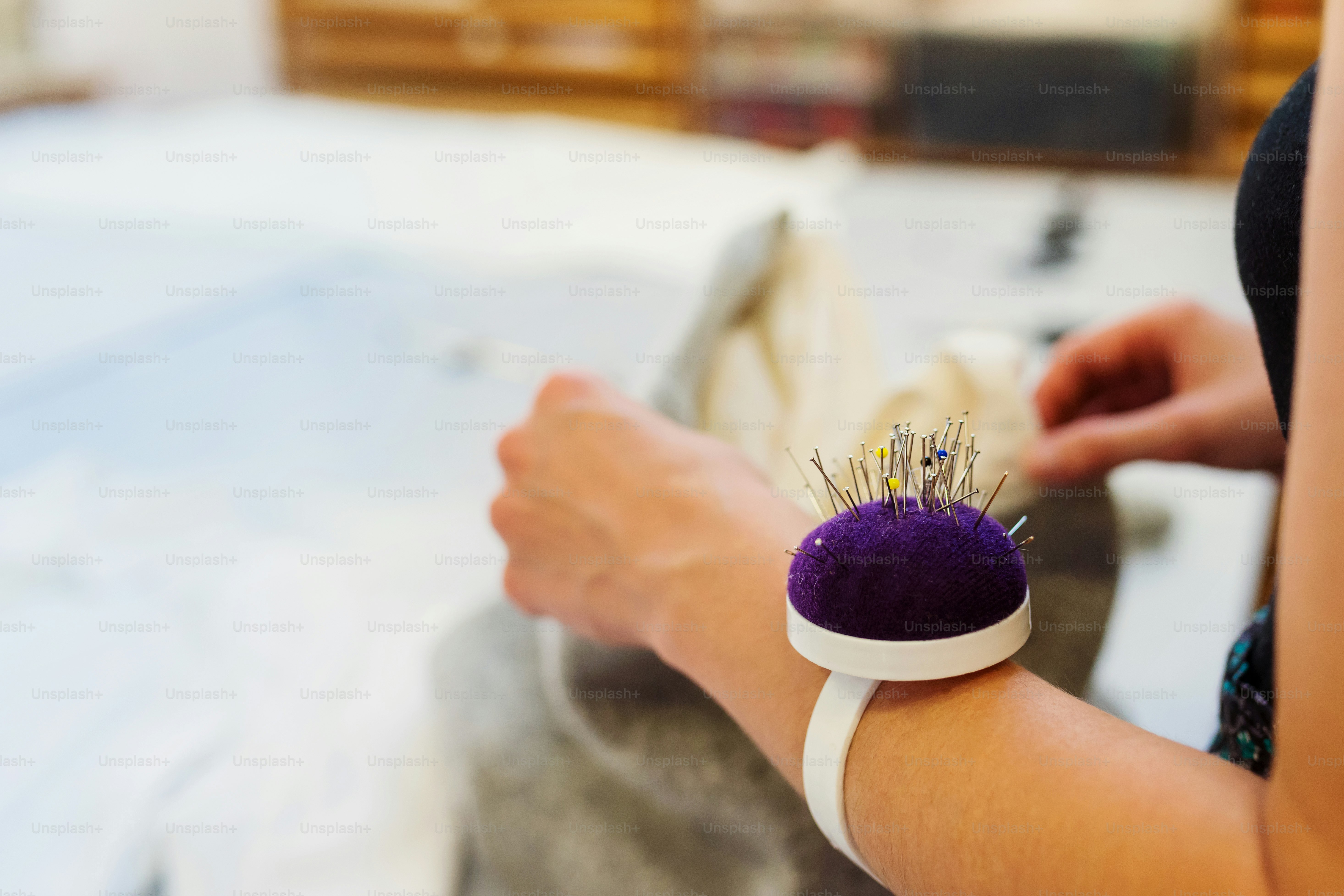 Nahaufnahme der Hände einer nicht wiederzuerkennenden Schneiderin mit Nadelkissen bei der Handarbeit