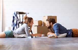 Joven pareja casada que se muda a una casa nueva, tendida en el suelo cerca de cajas de cartón, descansando.