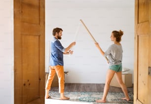 Young married couple moving in new house, fighting with rolls of wrapping paper.