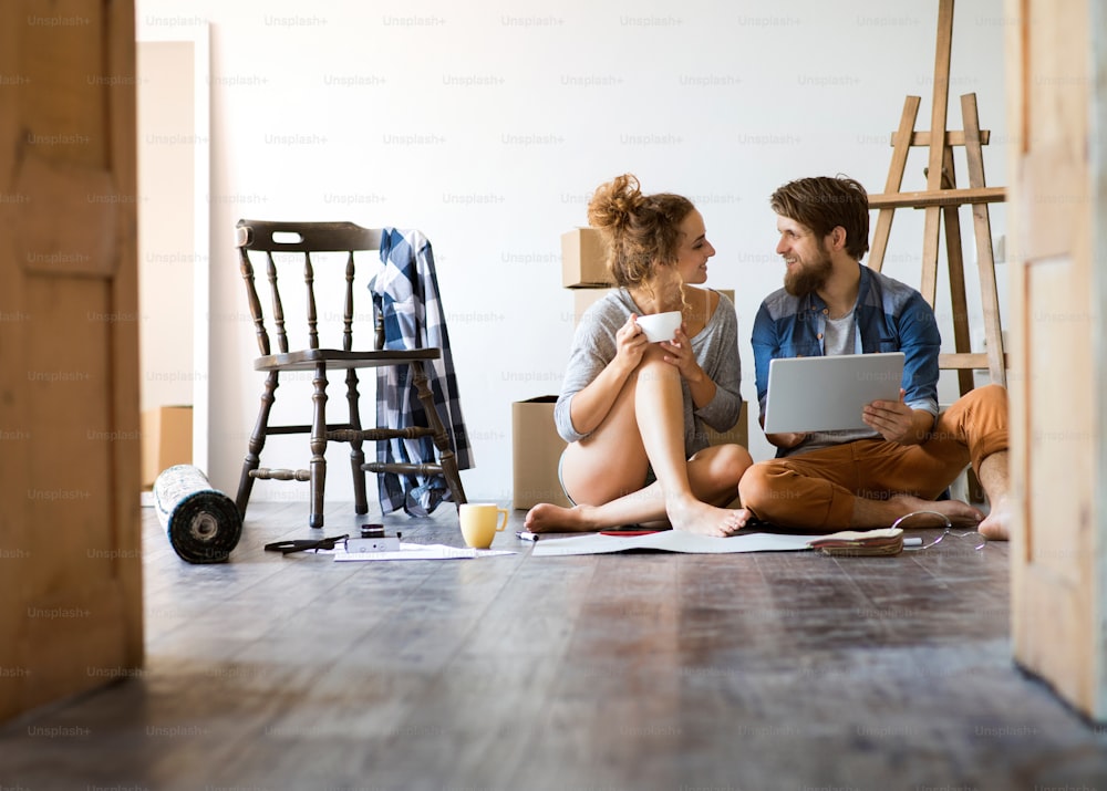 Young married couple with tablet moving in a new house, resting and making plans.
