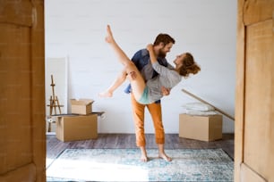 Joven pareja casada mudándose a una nueva casa, hombre llevando mujer en sus brazos.