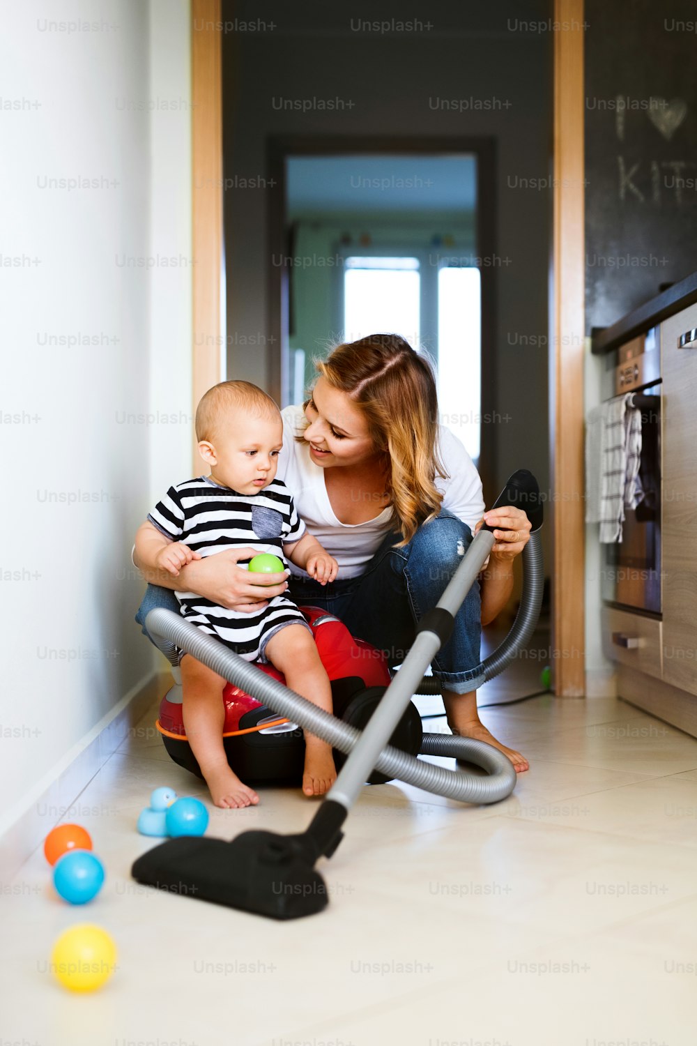 Beautiful young mother with a baby son doing housework. Beautiful woman and baby boy hoovering.