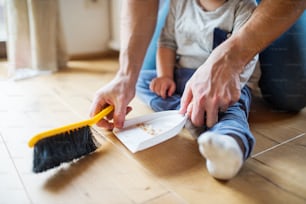 Unrecognizable father and toddler boy with brush and dustpan. Paternity leave.