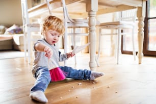 A cute toddler boy with brush and dustpan at home.