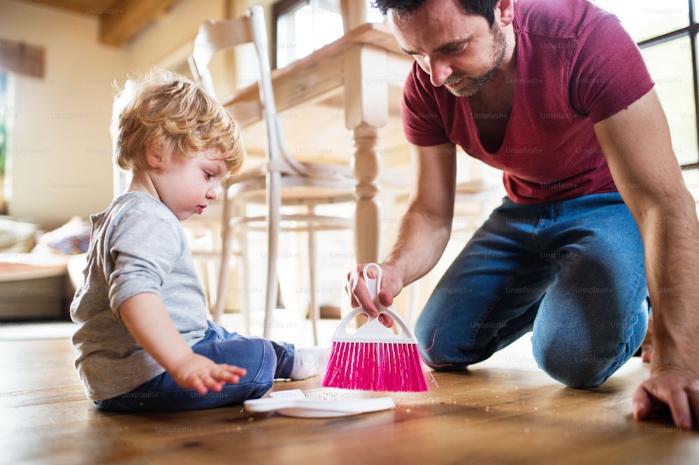 A handsome father and toddler boy with brush and dustpan. Paternity leave.