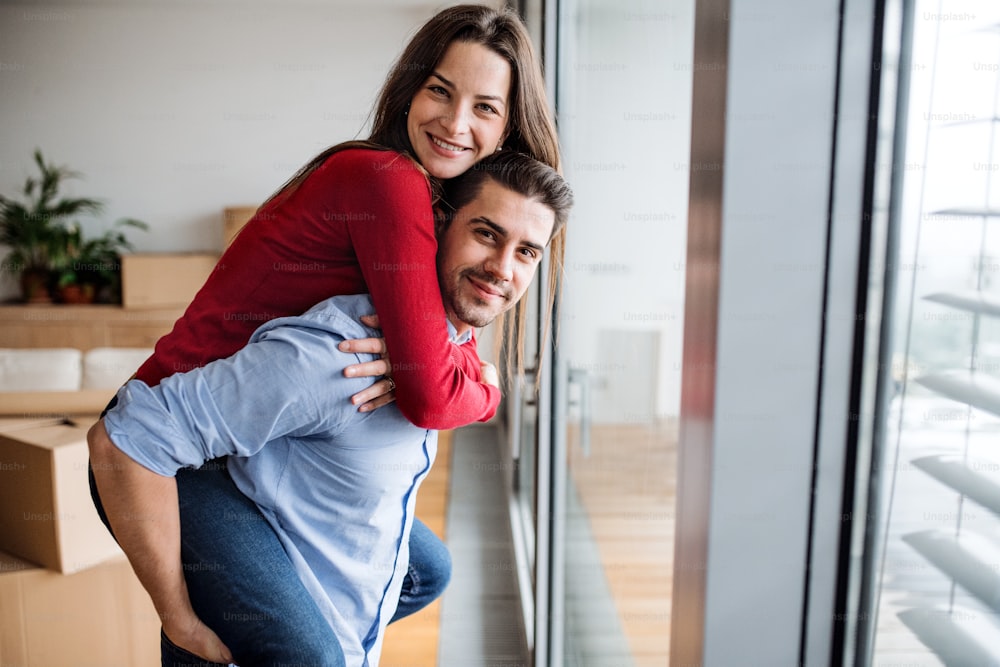 Young happy couple moving in a new home, having fun. A man giving a woman a piggyback ride.