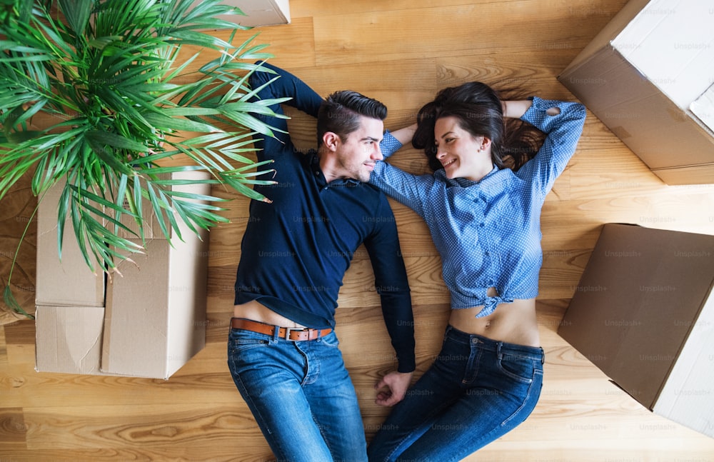 Une vue de dessus d’un jeune couple avec des boîtes en carton allongées sur le sol, emménageant dans une nouvelle maison.