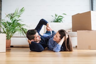 A young happy couple with a key and cardboard boxes lying on a floor, moving in a new home.