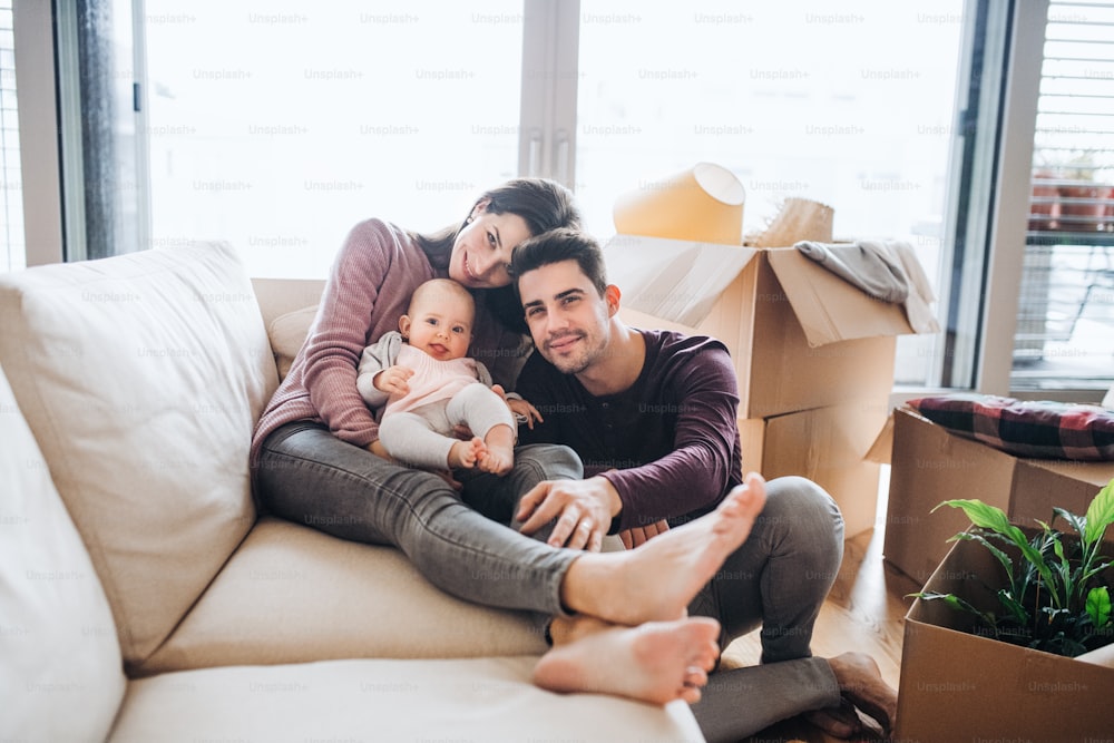 A portrait of happy young couple with a baby and cardboard boxes, moving in a new home.