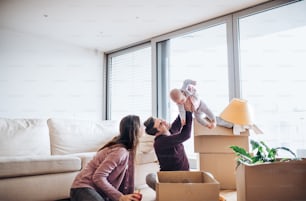 Young couple with a baby and cardboard boxes sitting on a floor, moving in a new home.
