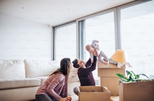 Jeune couple avec un bébé et des boîtes en carton assis sur un plancher, déménageant dans une nouvelle maison.