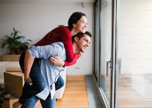 Young happy couple moving in a new home, having fun. A man giving a woman a piggyback ride.