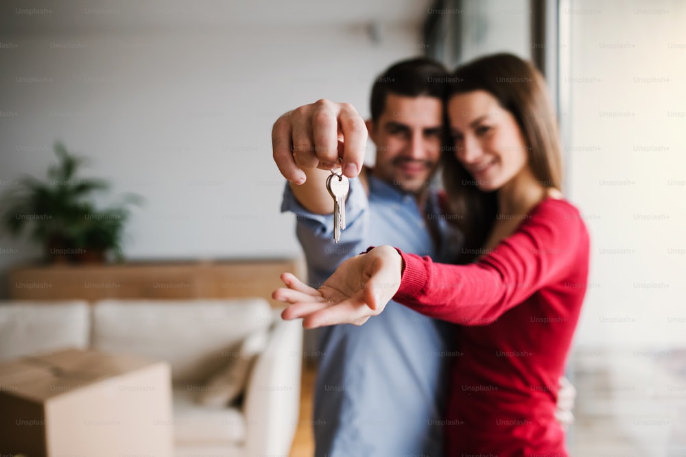열쇠와 골판지 상자를 들고 실내에 서서 새 집으로 이사하는 젊은 행복한 부부.