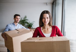 Joven pareja feliz que se muda a un nuevo hogar, sosteniendo cajas de cartón.