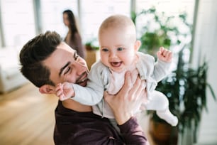A portrait of young happy father with a baby girl standing indoors in a room.