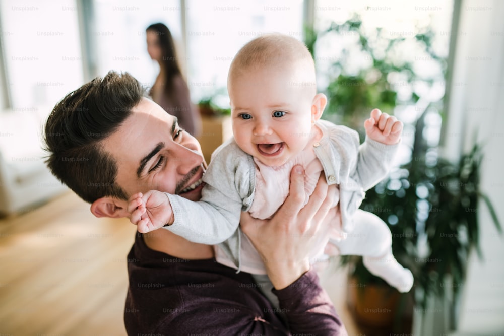 A portrait of young happy father with a baby girl standing indoors in a room.