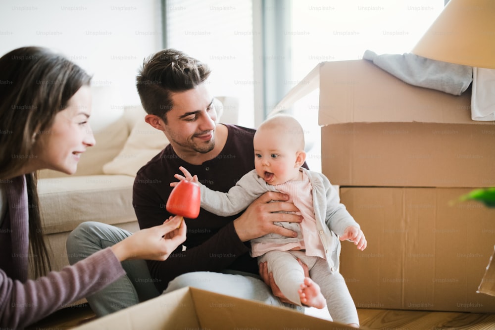 Jovem casal com um bebê e caixas de papelão sentado em um chão, movendo-se em uma nova casa.