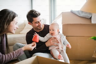 Junges Paar mit einem Baby und Pappkartons, die auf einem Boden sitzen und in ein neues Zuhause ziehen.