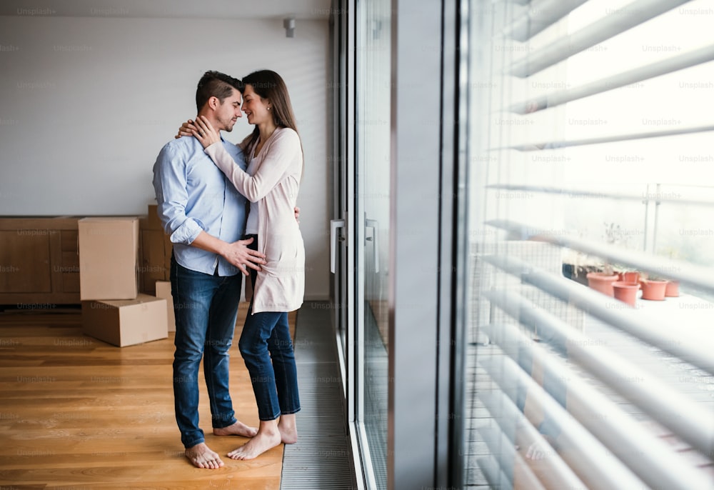 Jeune couple heureux avec des boîtes en carton qui déménagent dans une nouvelle maison, s’étreignant. Espace de copie.