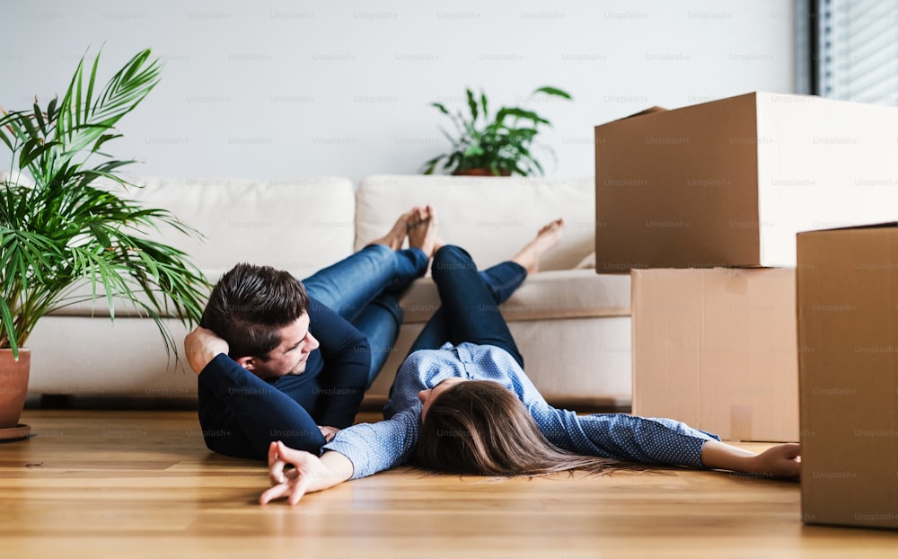 Um jovem casal com caixas de papelão deitado no chão, movendo-se em uma nova casa.