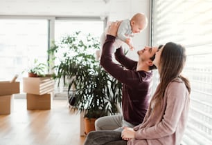 A portrait of happy young couple with a baby and cardboard boxes, moving in a new home.