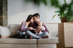 Ein Porträt eines glücklichen jungen Paares mit Baby und Pappkartons, das in ein neues Zuhause zieht.