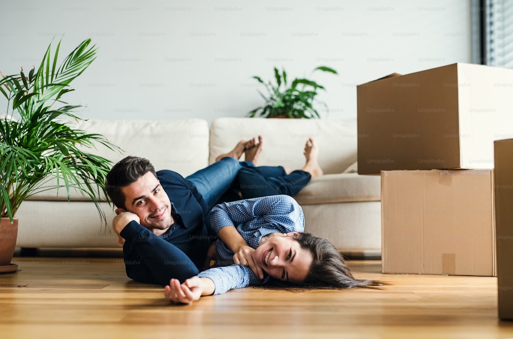 Una giovane coppia con scatole di cartone sdraiate sul pavimento, che si trasferiscono in una nuova casa.