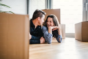 A young happy couple with a cup and cardboard boxes lying on a floor, moving in a new home.