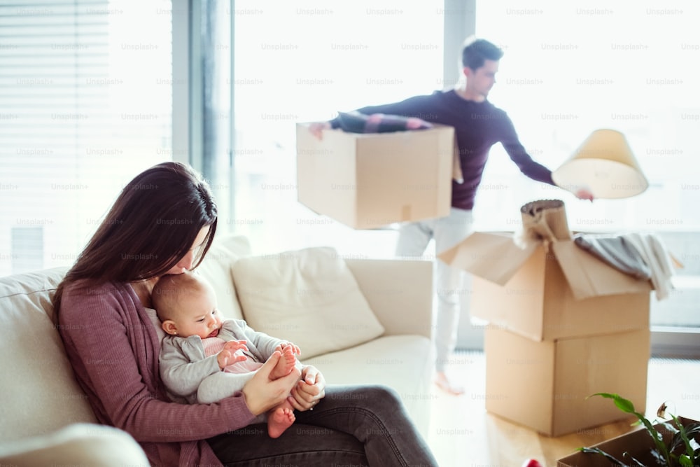 A portrait of happy young couple with a baby and cardboard boxes, moving in a new home.