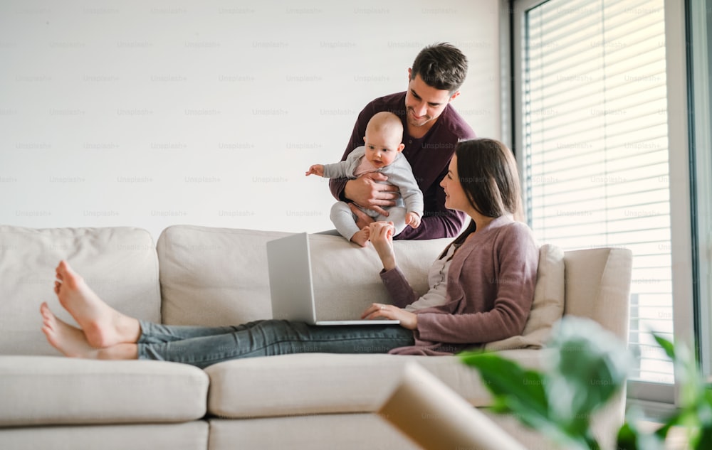 집에서 아기를 안고 있는 젊은 부부의 초상화는 노트북을 사용한다. 복사 공간.