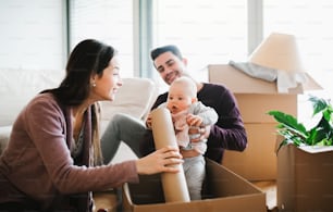 A portrait of happy young couple sitting on a sofa with a baby and cardboard boxes, moving in a new home.