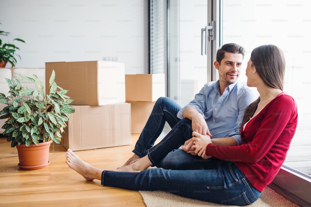 Jeune couple amoureux emménageant dans une nouvelle maison, assis par terre et se regardant.