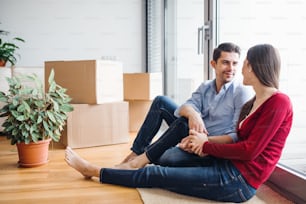Jeune couple amoureux emménageant dans une nouvelle maison, assis par terre et se regardant.