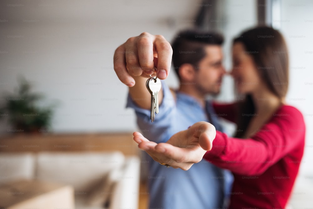 Una giovane coppia felice con una chiave e scatole di cartone in piedi in casa, trasferendosi in una nuova casa.