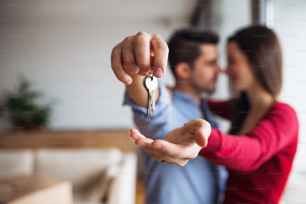 A young happy couple with a key and cardboard boxes standing indoors, moving in a new home.