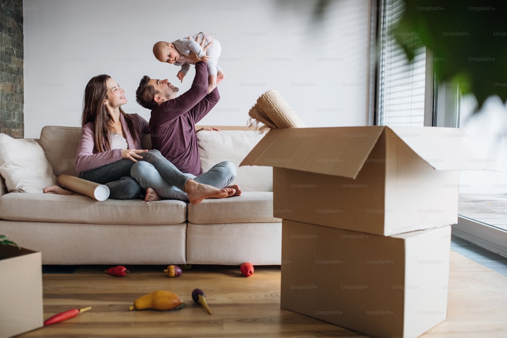 Un ritratto di una giovane coppia felice con un bambino e scatole di cartone, che si trasferiscono in una nuova casa.
