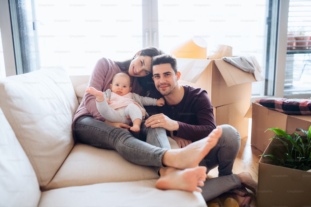 Um retrato de um jovem casal feliz com um bebê e caixas de papelão, movendo-se em uma nova casa.