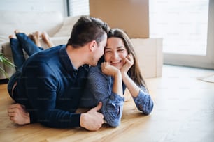 Una joven pareja feliz con una taza y cajas de cartón tiradas en el suelo, mudándose a un nuevo hogar.