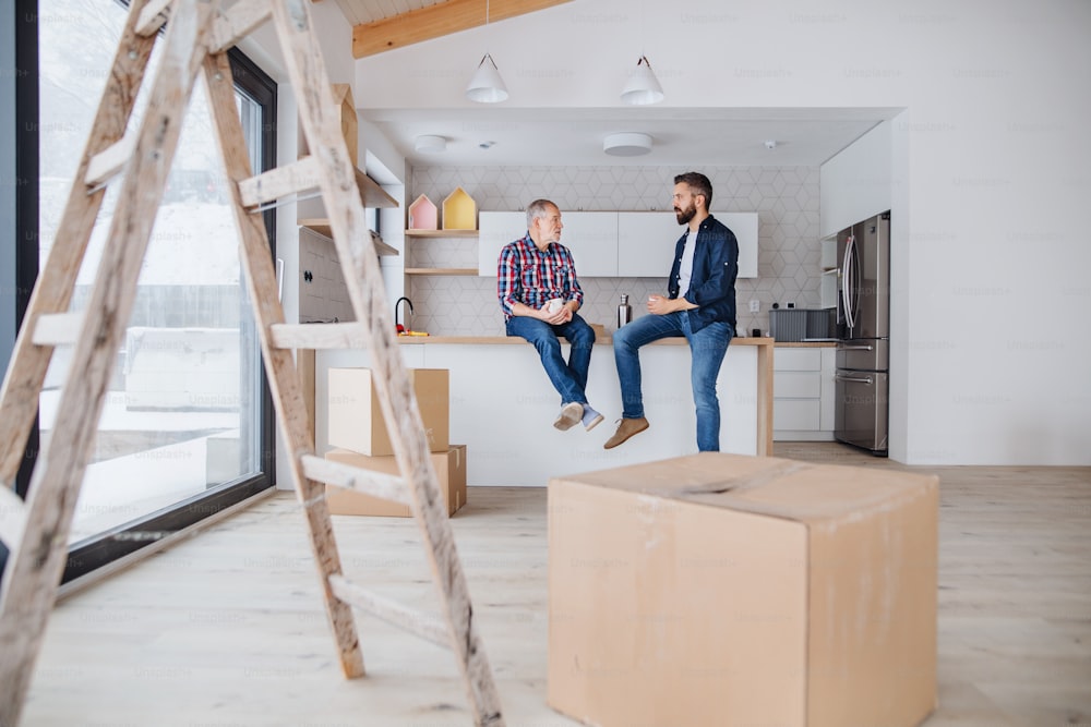 A portrait of mature man with his senior father drinking coffee when furnishing new house, a new home concept. Copy space.