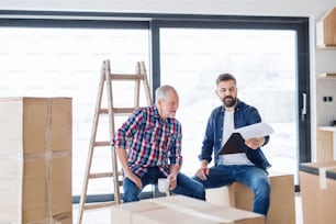 A cheerful senior man helping his mature son with furnishing new house, a new home concept.