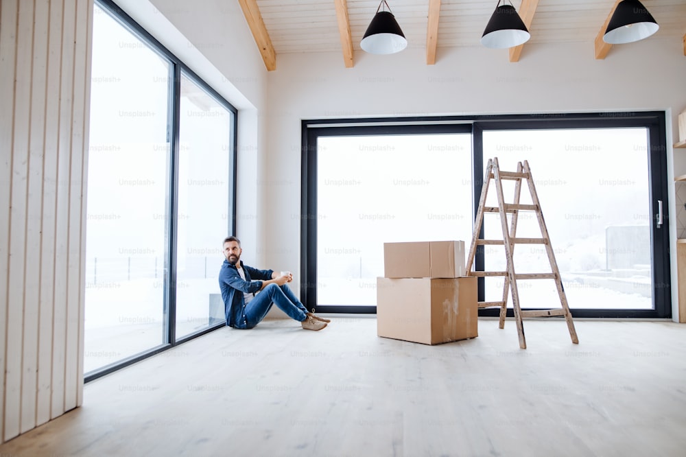 Um homem maduro com caixas de papelão sentado no chão, mobiliando nova casa. Um novo conceito de casa. Espaço de cópia.