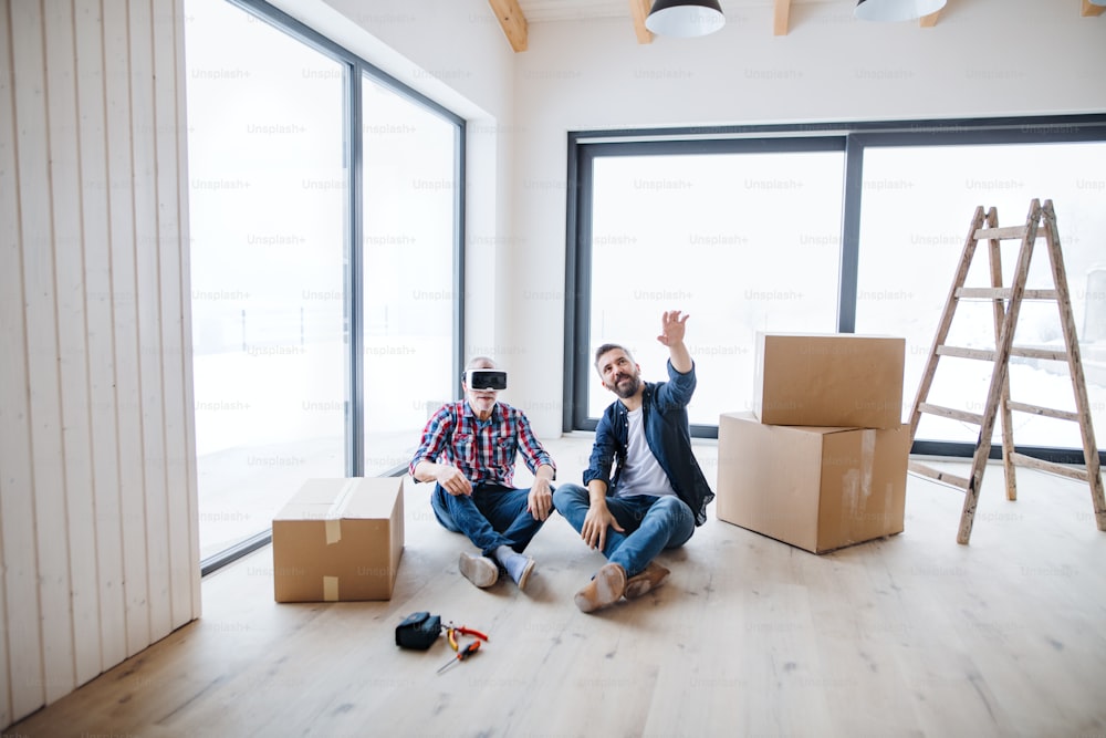 Un hombre maduro con gafas VR y su padre mayor amueblando una nueva casa, un nuevo concepto de hogar.