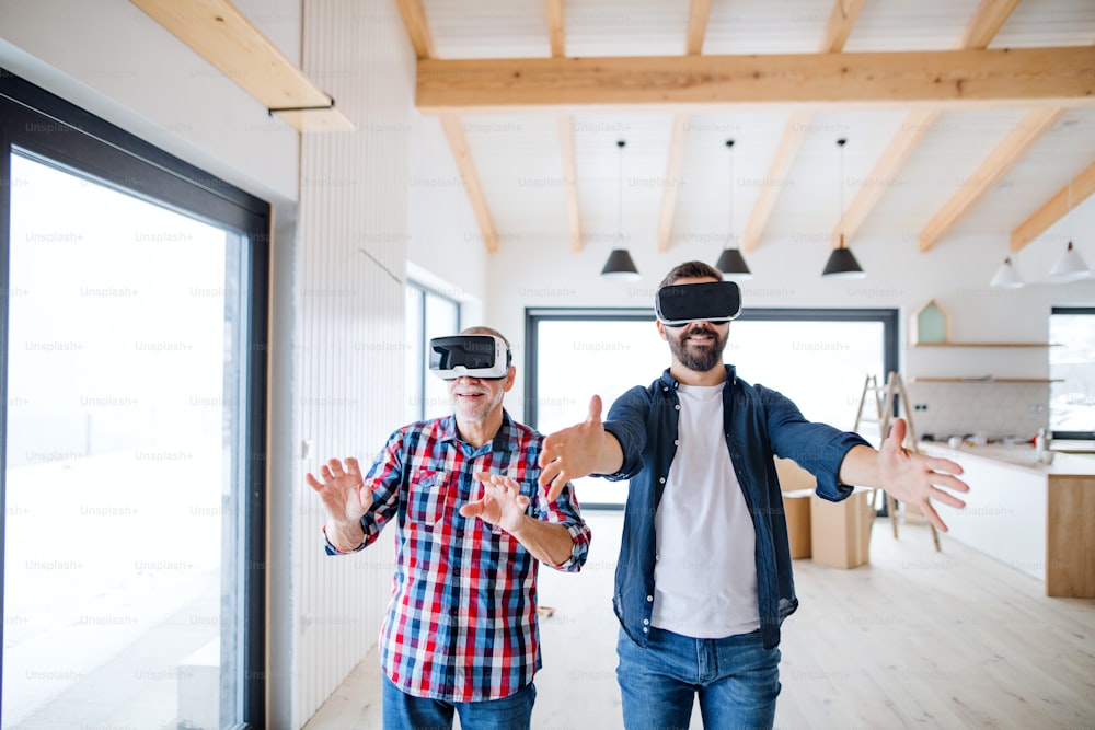 A mature man with VR goggles and his senior father furnishing new house, a new home concept.